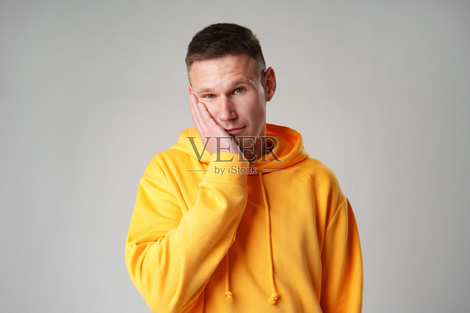灰色背景上穿着黄色连帽衫的年轻人的脸部手掌手势照片摄影图片