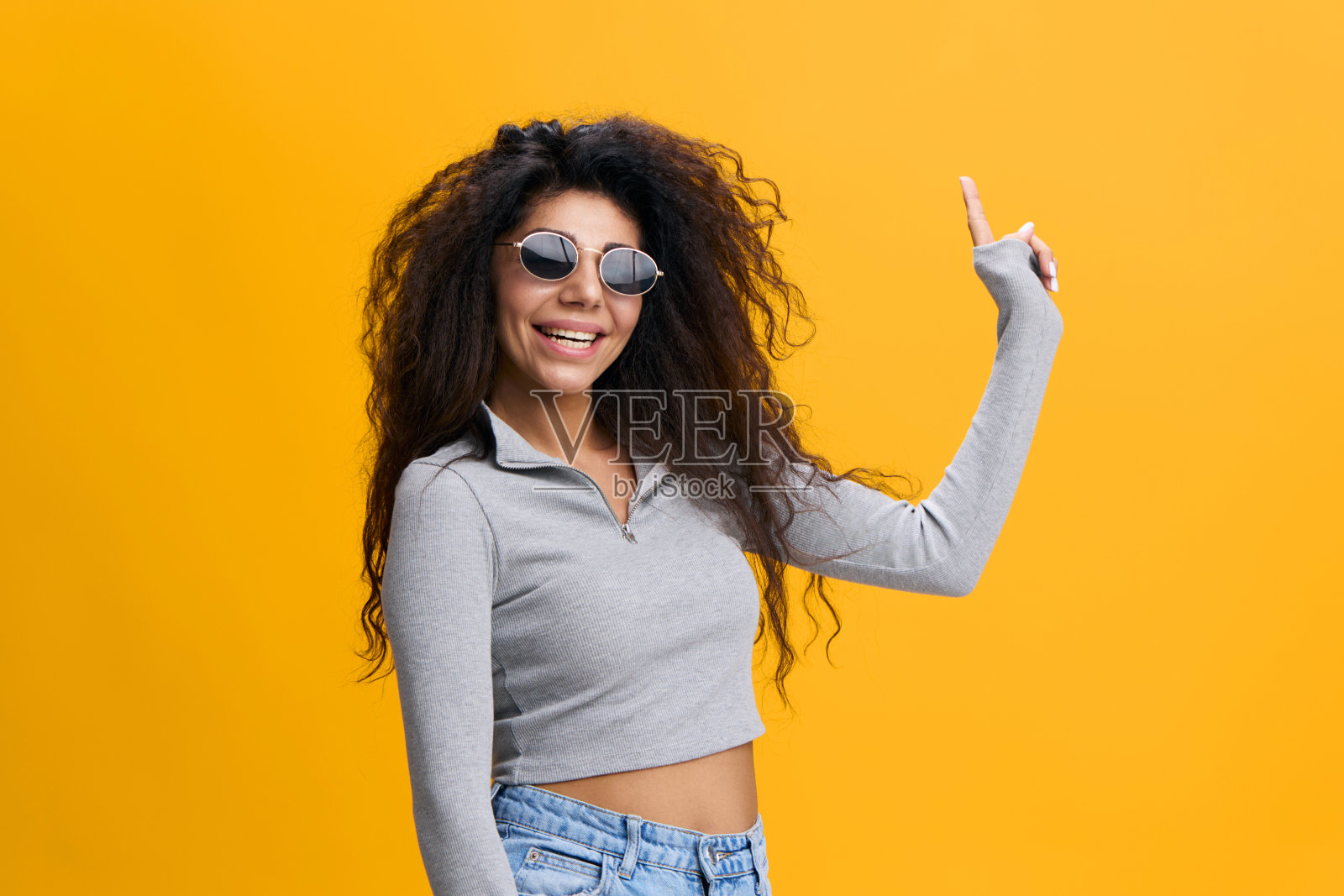 嘿，看看这个。开朗漂亮的拉丁女性，戴着墨镜，留着非洲式发型，微笑着。手指向上，显示广告的空白空间，在黄色背景上保持孤立。复制空间，空闲位置，横幅照片摄影图片