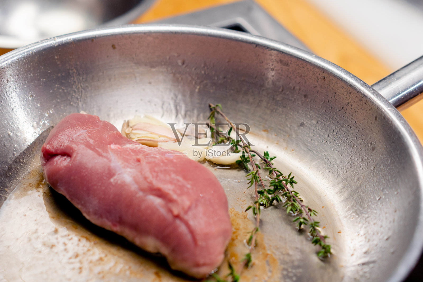在热煎锅上加入迷迭香的粉色鸭胸肉的特写照片摄影图片
