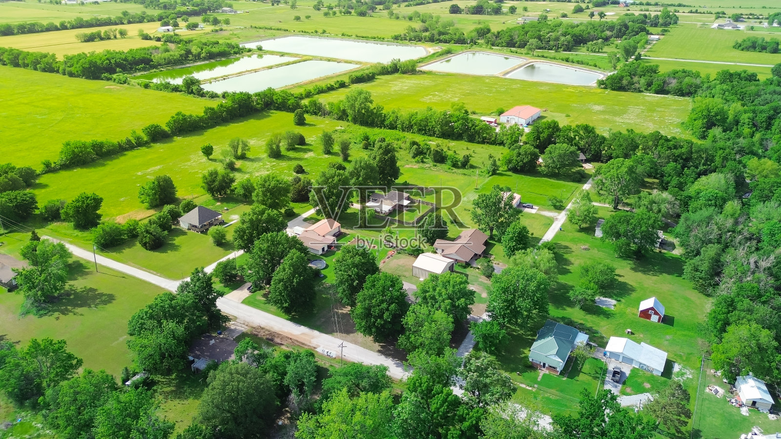 在大片土地上的农舍，周围环绕着郁郁葱葱的绿树、储藏棚和大片农田、池塘系统，在俄克拉何马州的Fairland，美国农村工业鸟瞰草地照片摄影图片