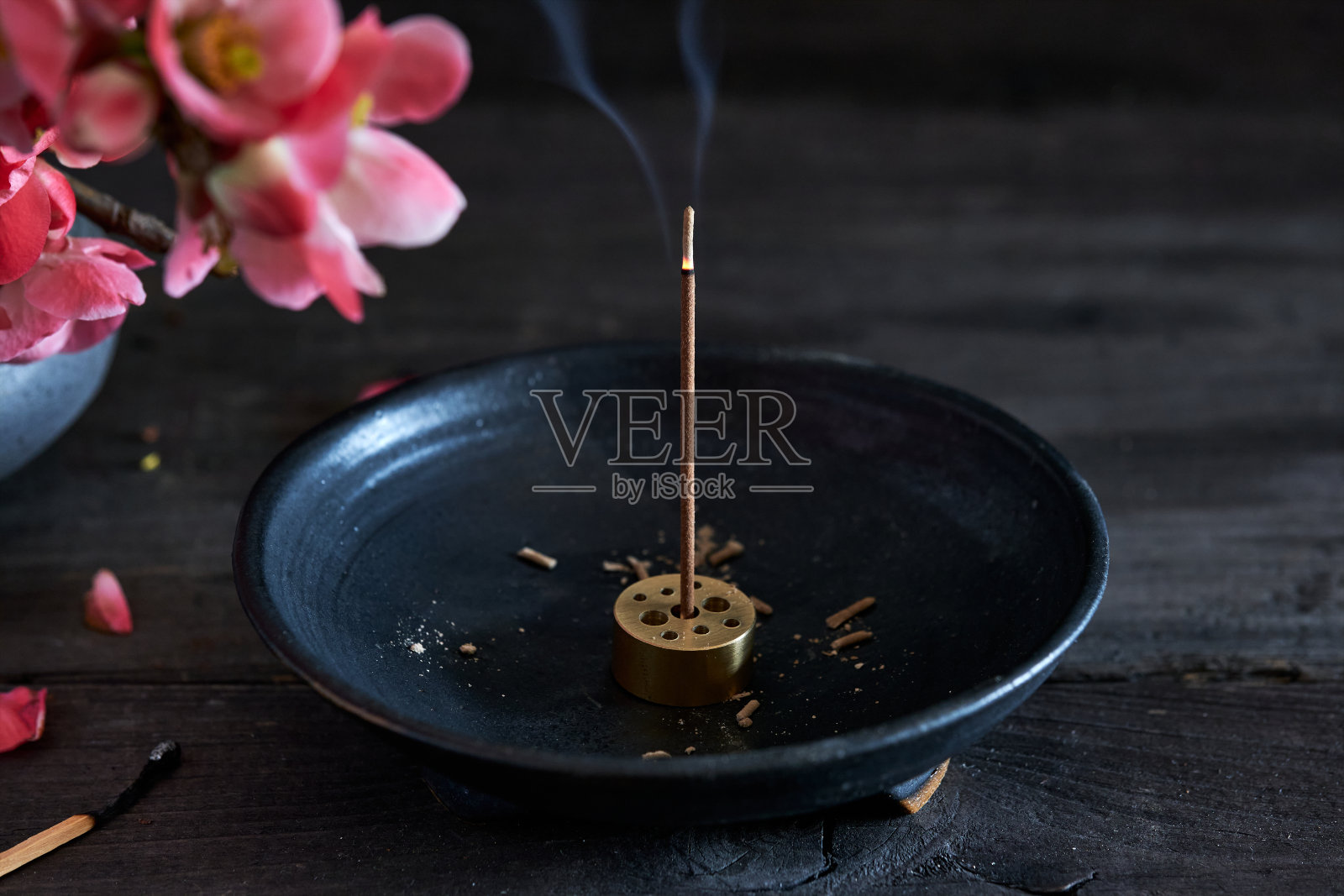 在圆香炉和花瓶上燃烧着日本香，花瓶上有粉红色的日本榅桲树枝照片摄影图片