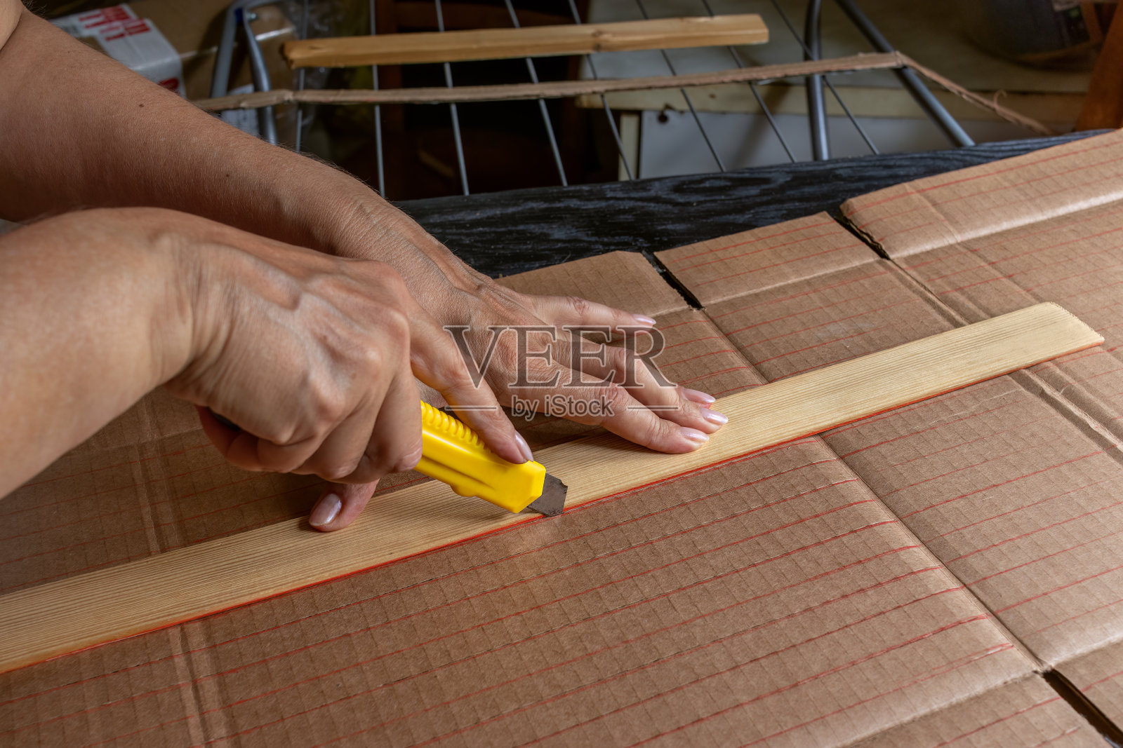 特写，一个女人的手沿着标记用文具刀切割瓦楞纸板条。概念回收包装成有用的家居用品，DIY。照片摄影图片