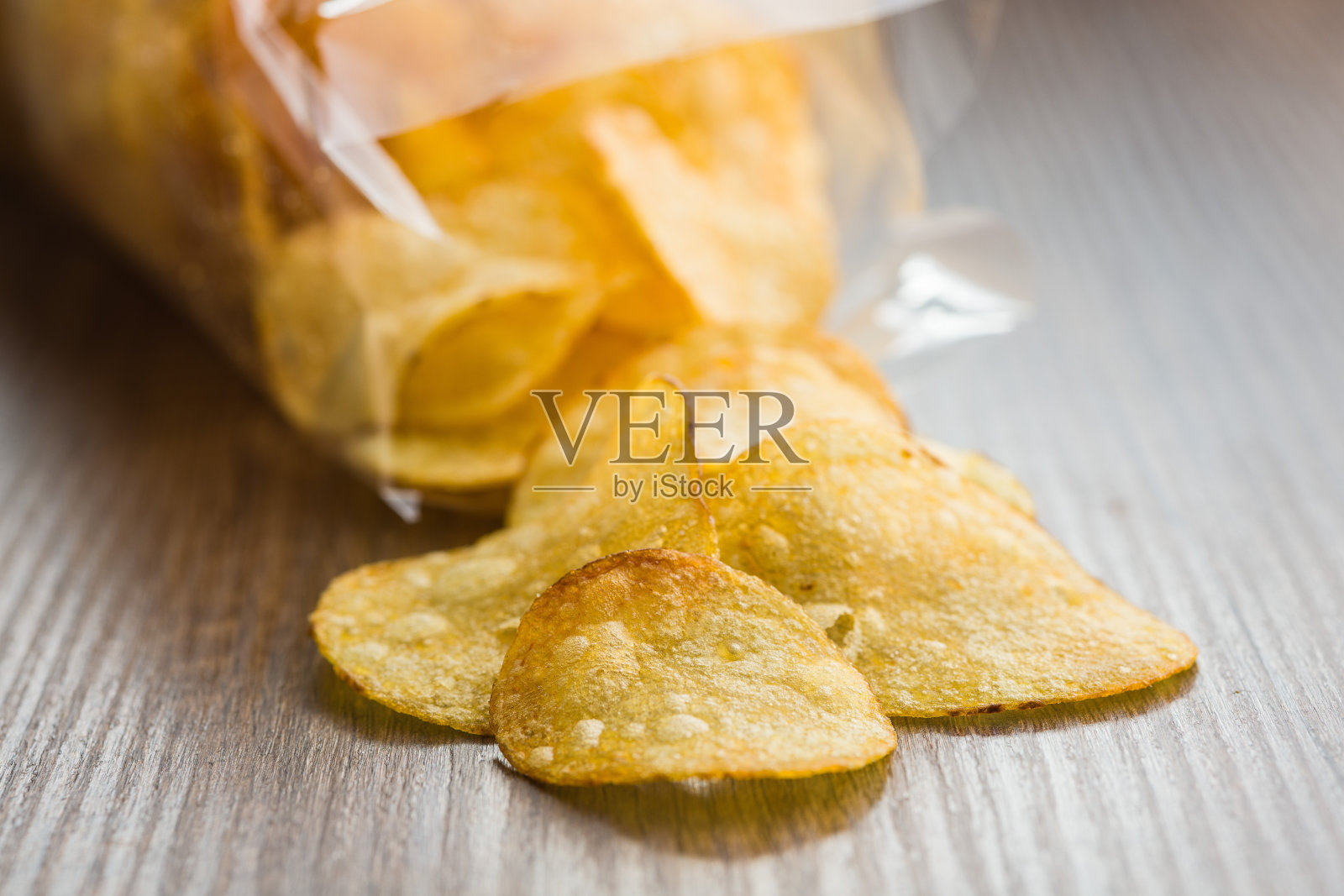 脆皮薯片从一个塑料袋里洒在木桌上照片摄影图片