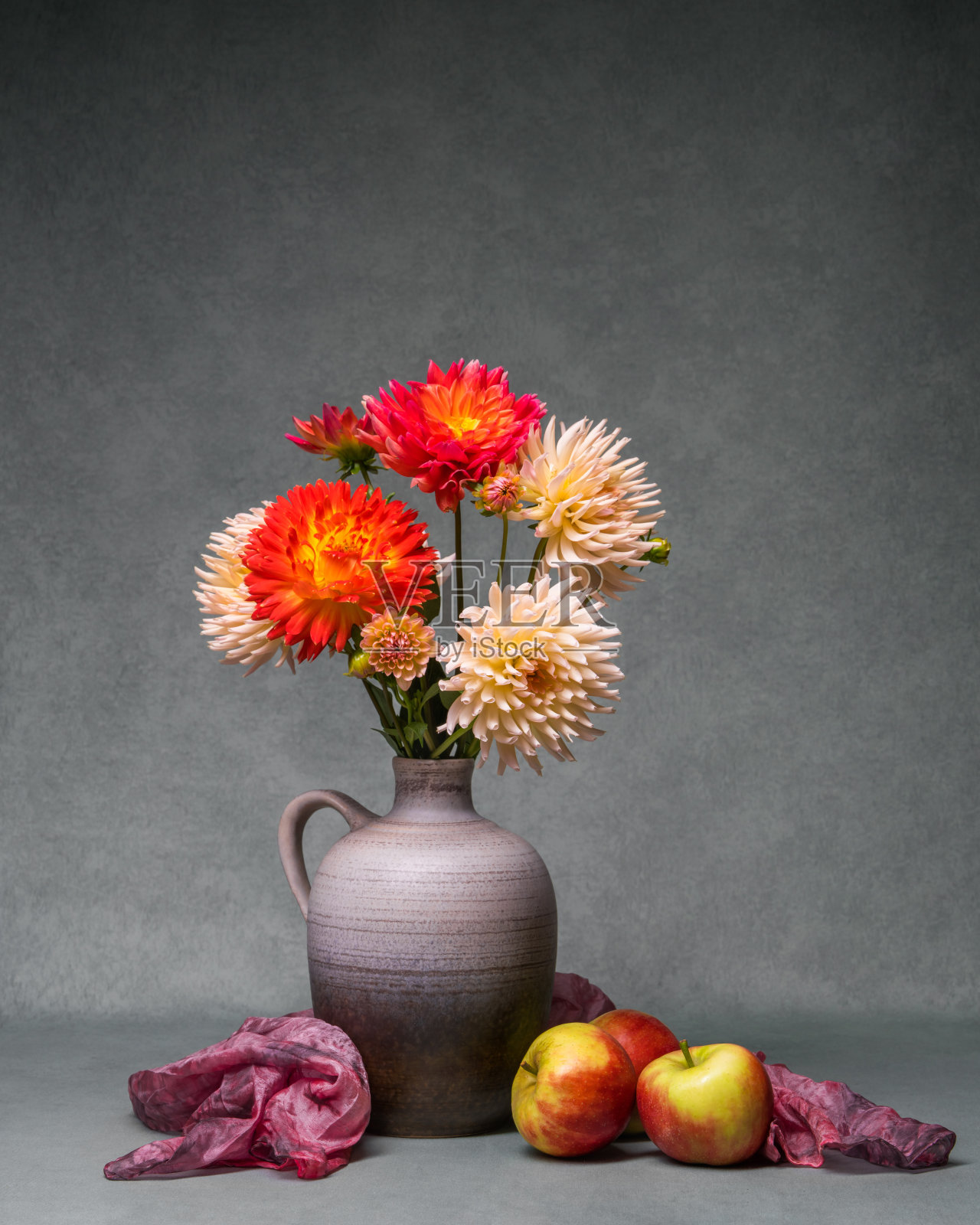灰色背景上，花瓶里插着一束鲜艳的花束，旁边放着三个红苹果。五彩缤纷的秋天静物与杂色大丽花。明信片，祝贺，祝福照片摄影图片