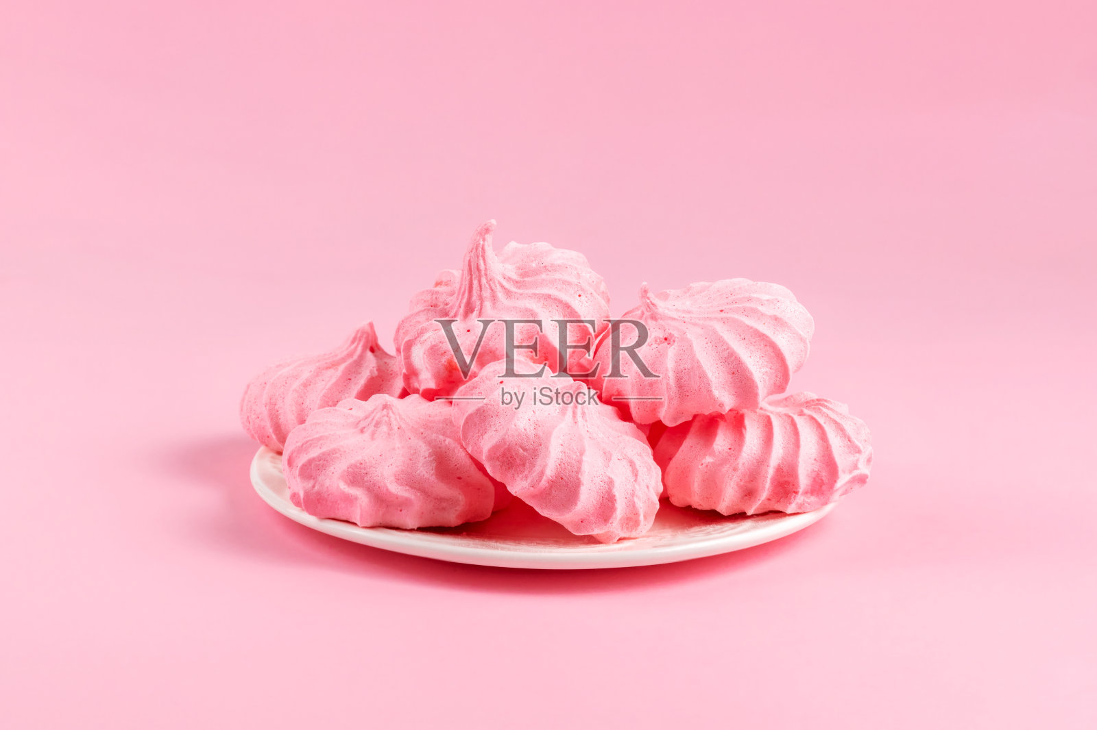 白色盘子里放着粉嫩的蛋白酥饼。甜的甜点。在粉红色背景上，复制空间照片摄影图片