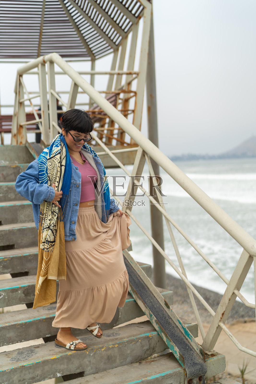 年轻女子走下通往海滩的楼梯。照片摄影图片