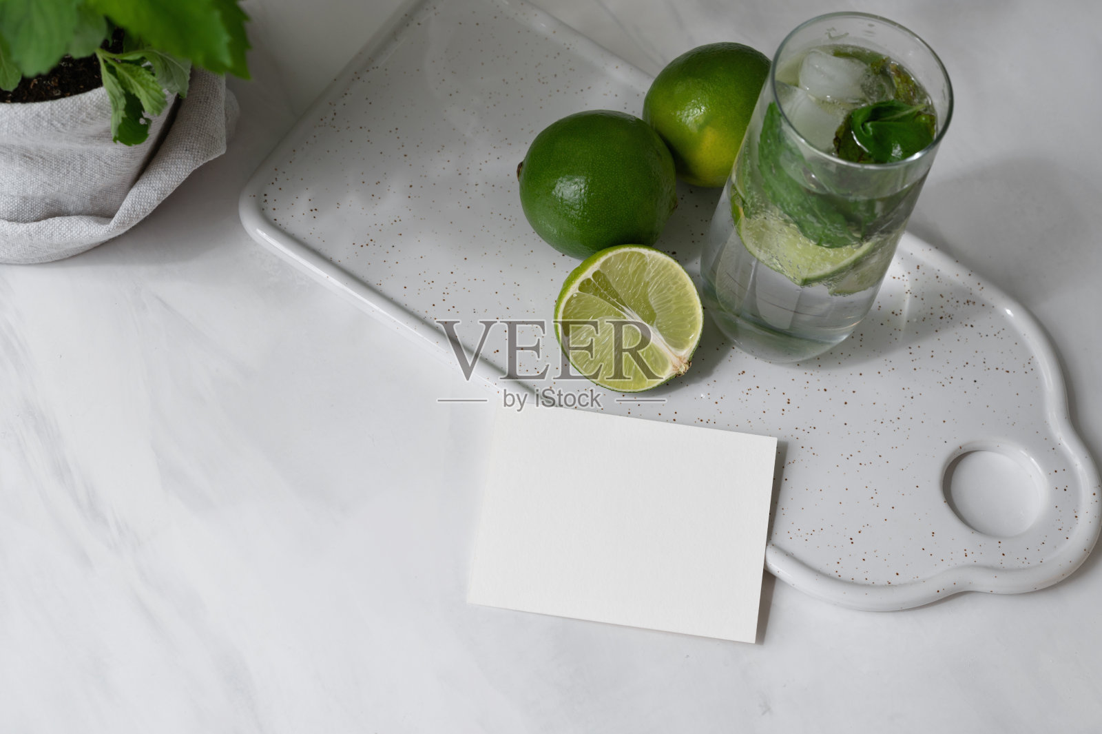空白的纸卡模型，绿色的酸橙和莫吉托鸡尾酒饮料在中性白色的桌子背景，夏季邀请或名片设计模板照片摄影图片
