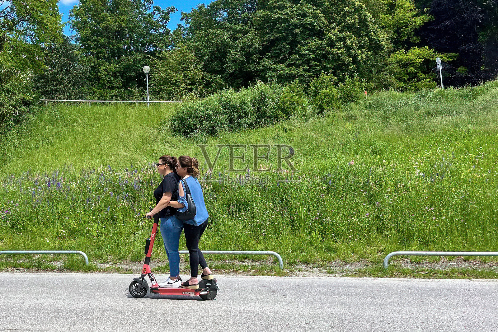 夏天，妇女们骑着摩托车，背景是绿树和鲜花盛开的草地。健康生活方式理念照片摄影图片