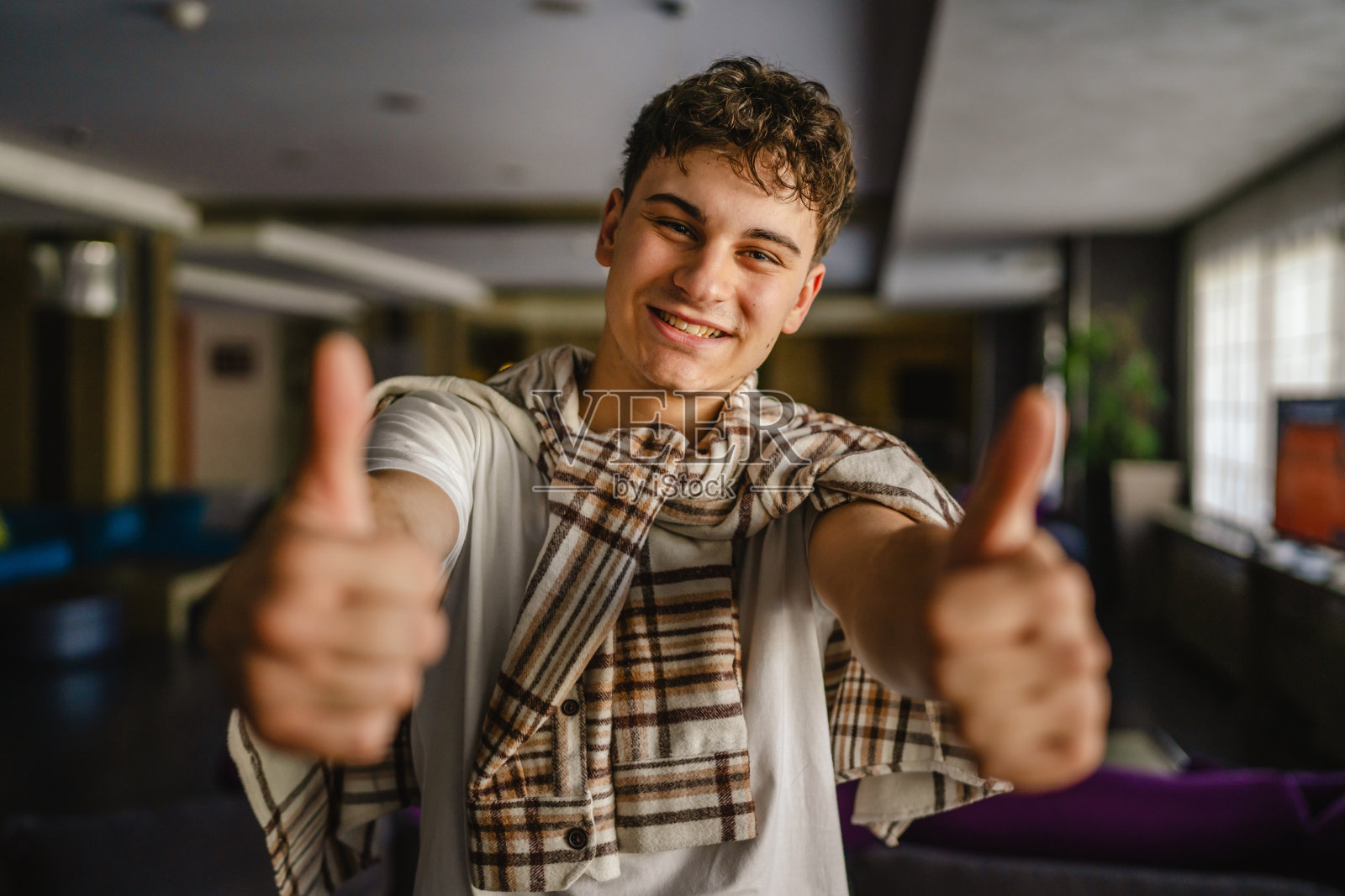 年轻人的肖像站在室内，双手竖起大拇指照片摄影图片