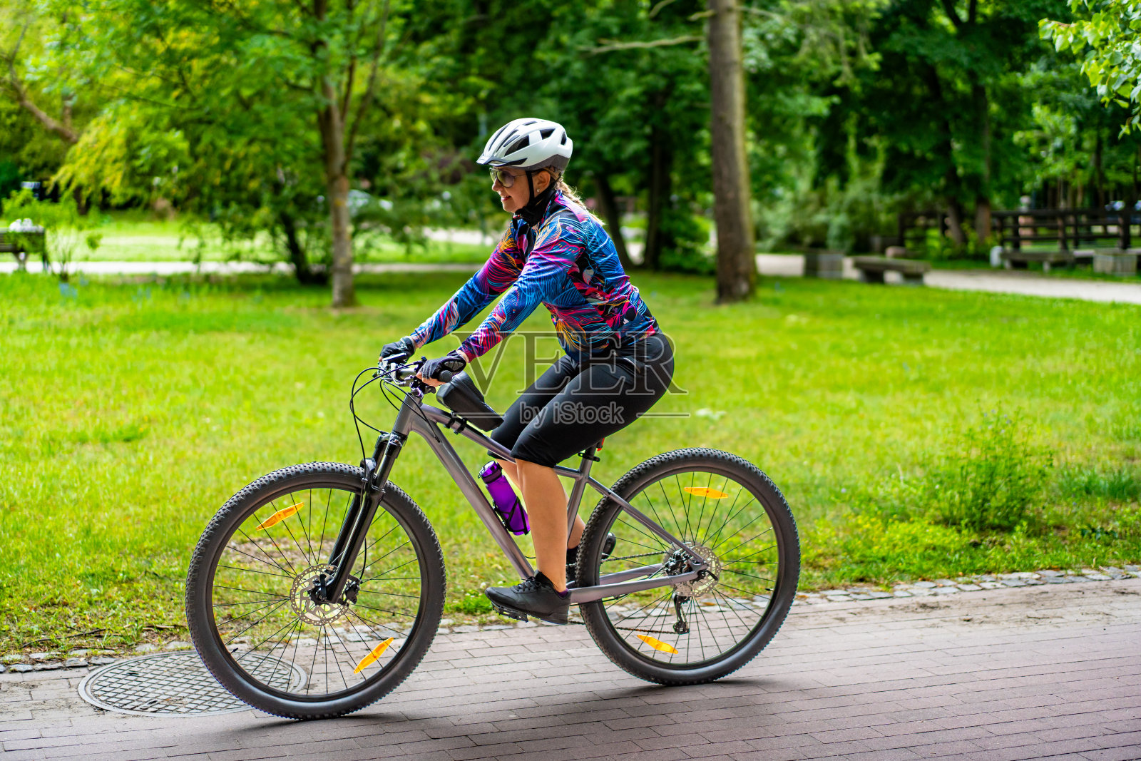 城市自行车训练。年轻快乐的女人戴着白色头盔，穿着彩色衬衫和黑色短裤在城市的自行车道上骑自行车。春天在户外运动。健康的生活方式照片摄影图片