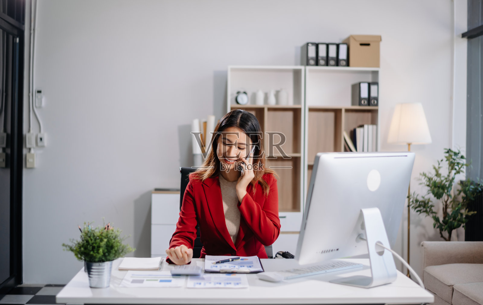 年轻漂亮的女人坐在现代办公室的白色办公桌旁，在平板电脑和笔记本电脑上打字照片摄影图片