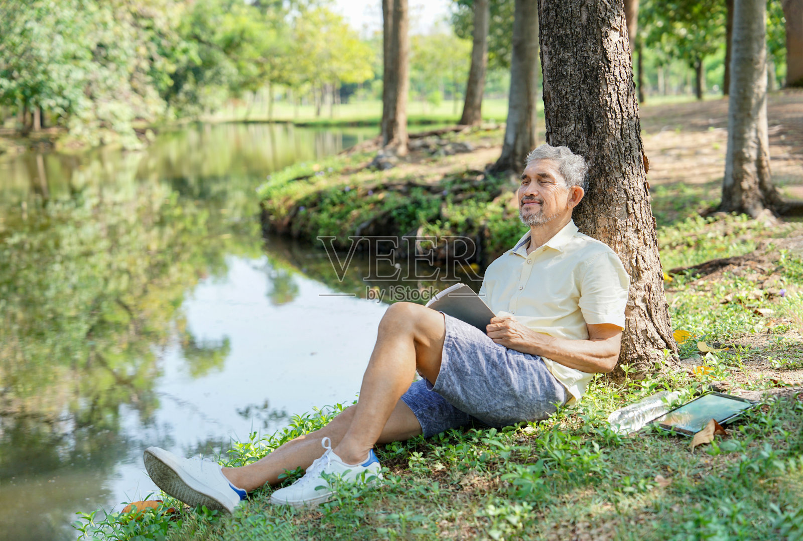 亚洲老人在树下看书时睡着了，老年人在自然公园休息，照片摄影图片