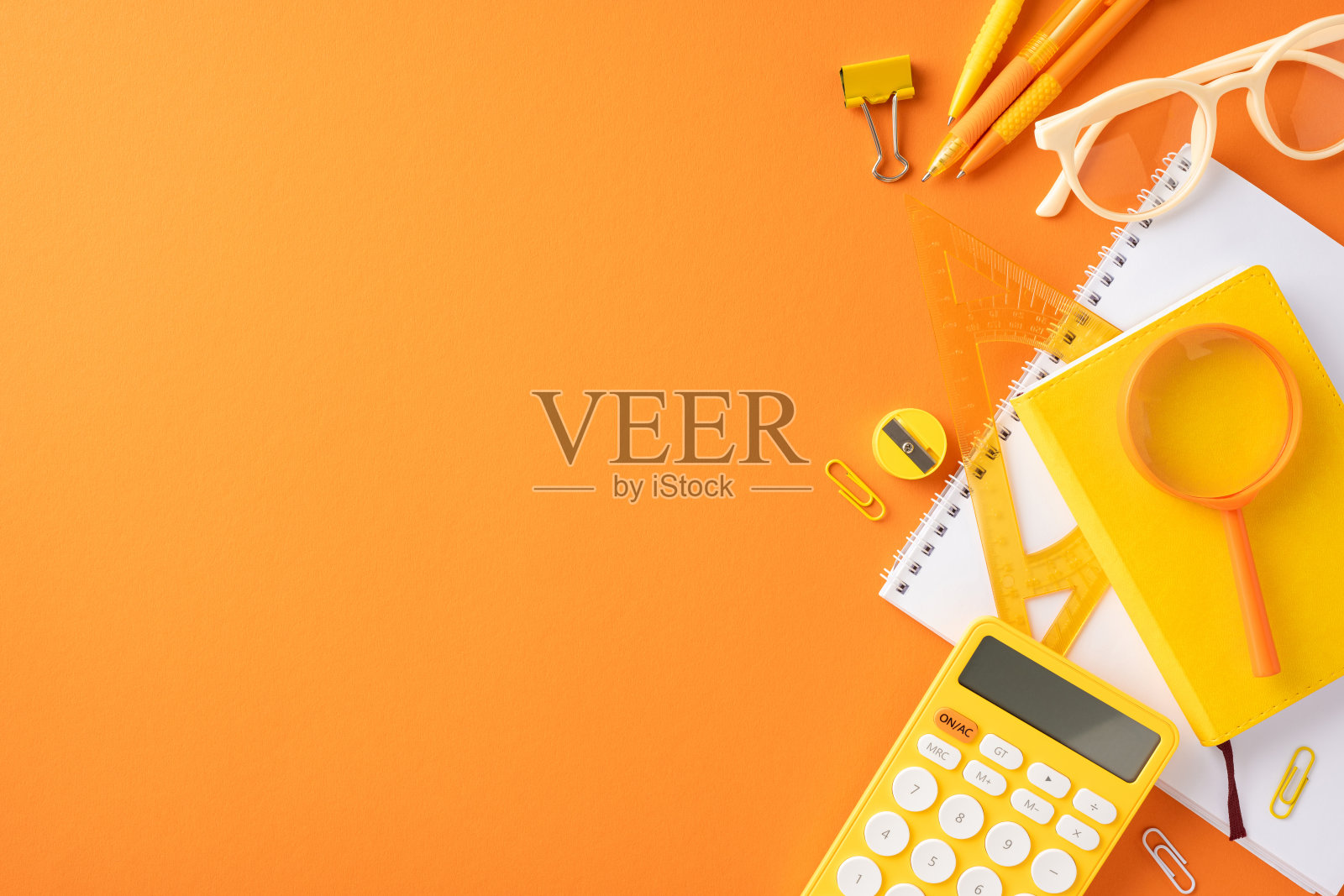 橙色背景上的黄色学习用品，包括计算器、放大镜和笔记本照片摄影图片