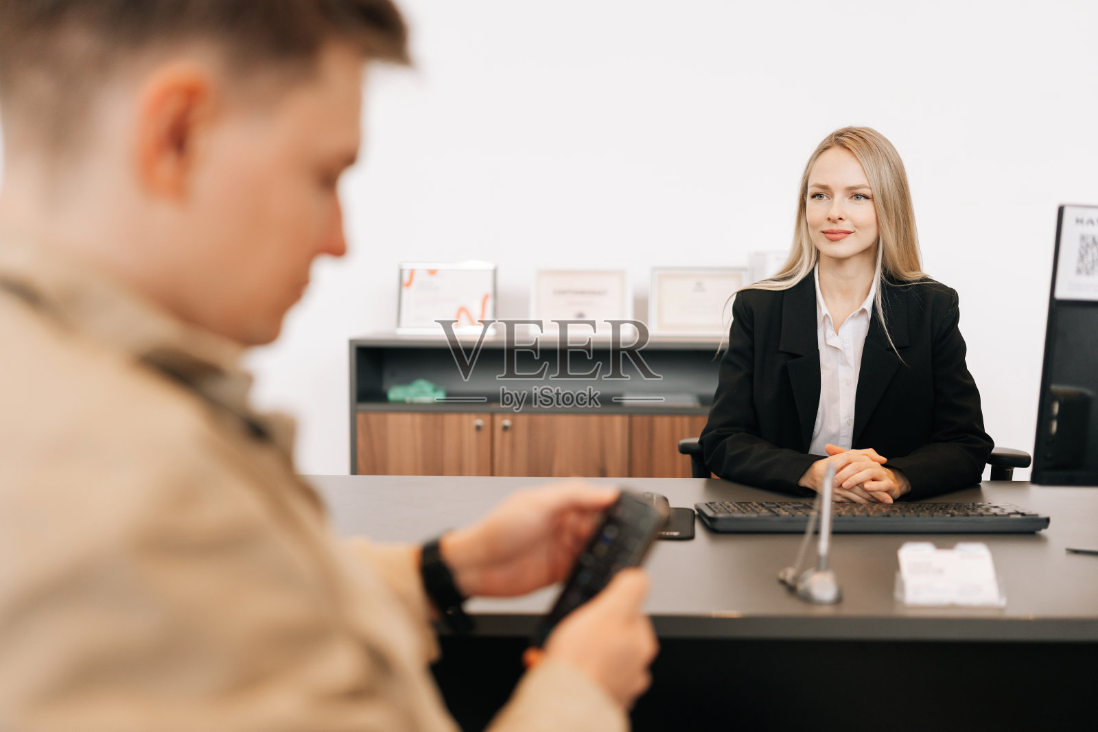 商务会议期间，无法辨认的男性客户与金发女经理坐在桌边使用手机的后视图。照片摄影图片