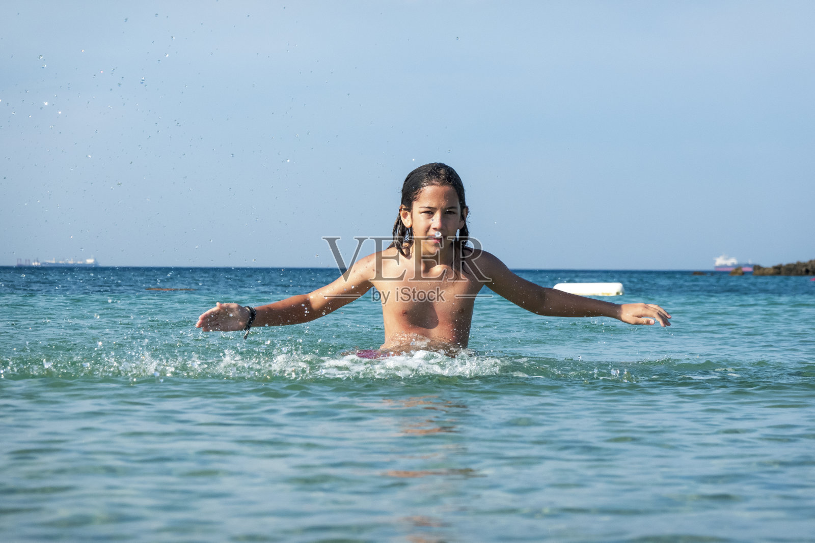 他用手在海里泼水。一个夏天的早晨。忒涅多斯岛。爱琴海北部，12岁的帅哥。长头发的照片摄影图片