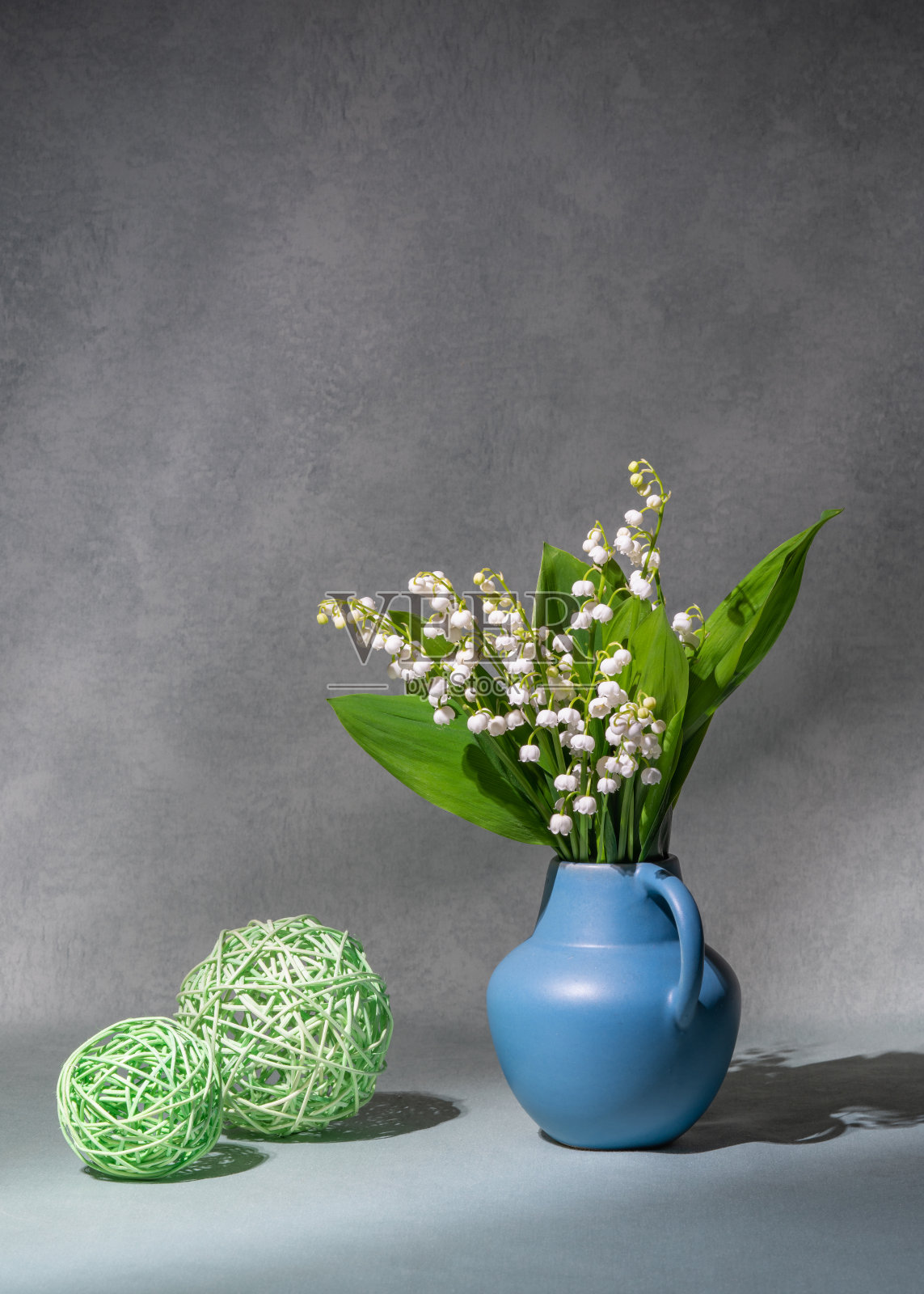 一束春天的花，蓝色花瓶里的铃兰，在灰色的背景上。附近有两个绿色的球。静物画，明信片，复印空间照片摄影图片