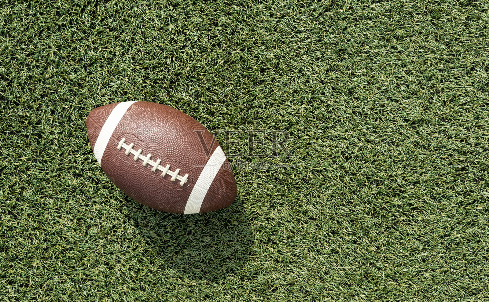 绿色足球场上的棕色皮革美式足球照片摄影图片