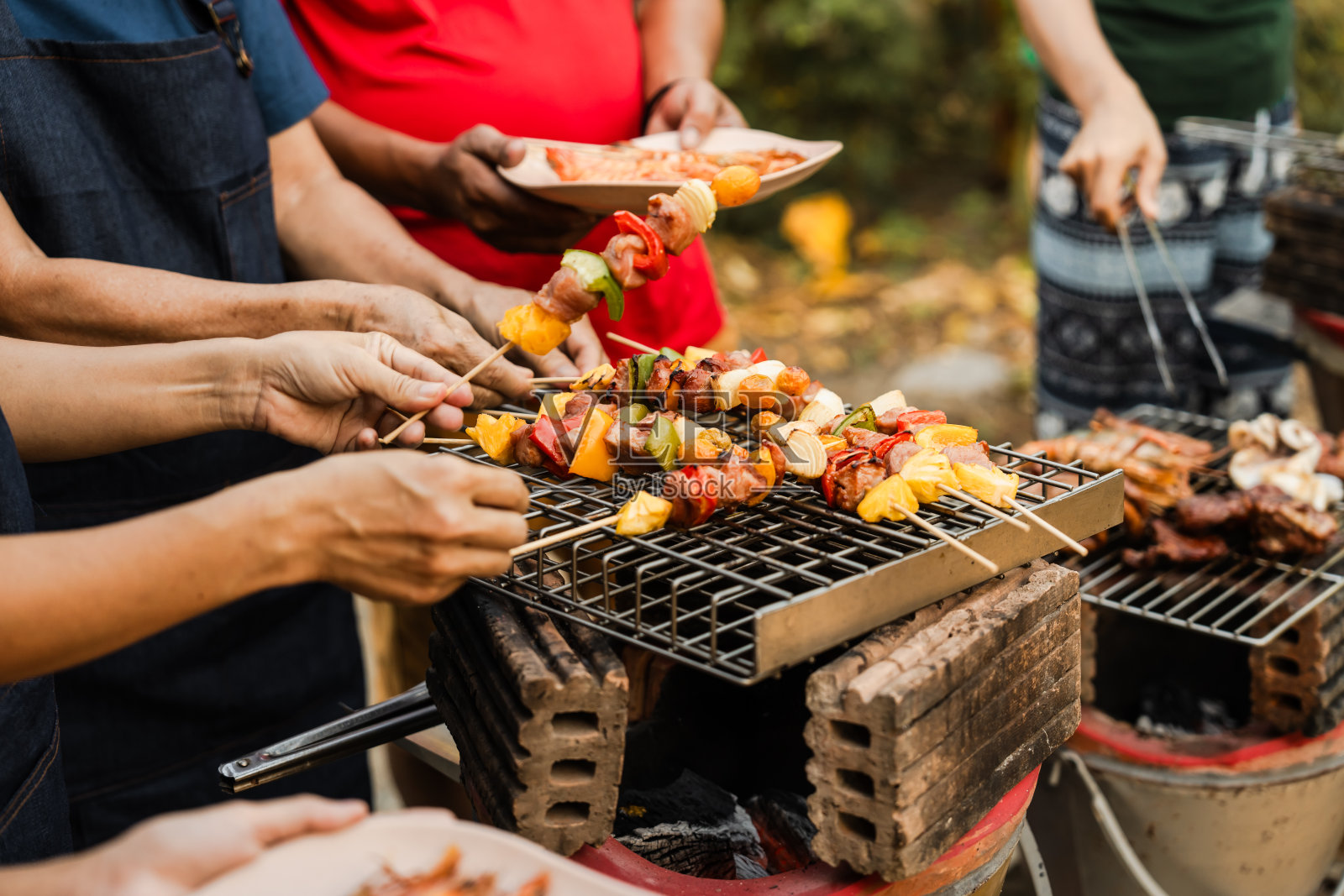 串着五颜六色的蔬菜和烤肉，家人和朋友聚在一起，享受着阳光明媚的户外大餐。烧烤聚会，烧烤周末，合家欢乐。照片摄影图片