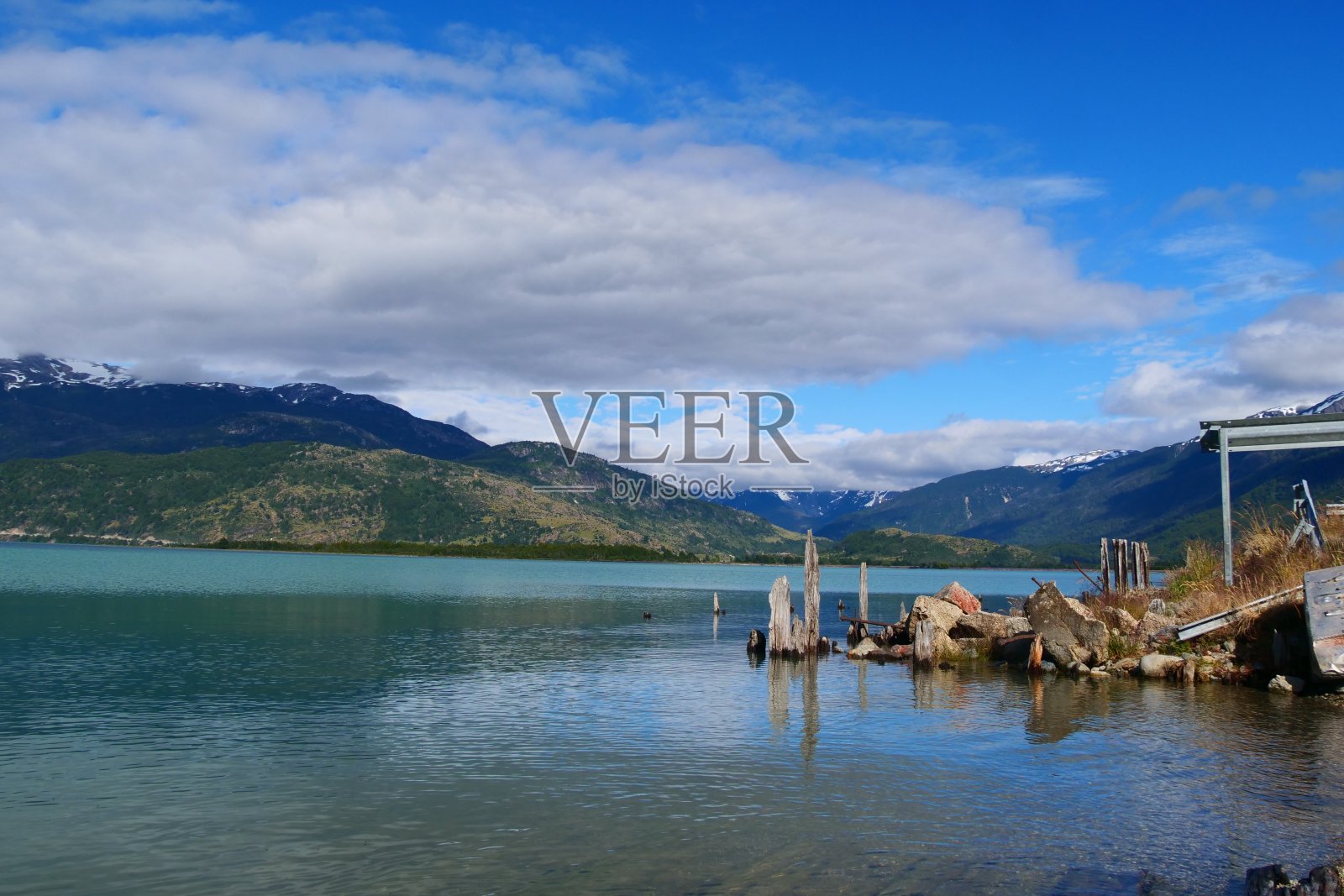 在多云的日子里，在大山环绕的湖边，腐烂的木头和岩石。照片摄影图片