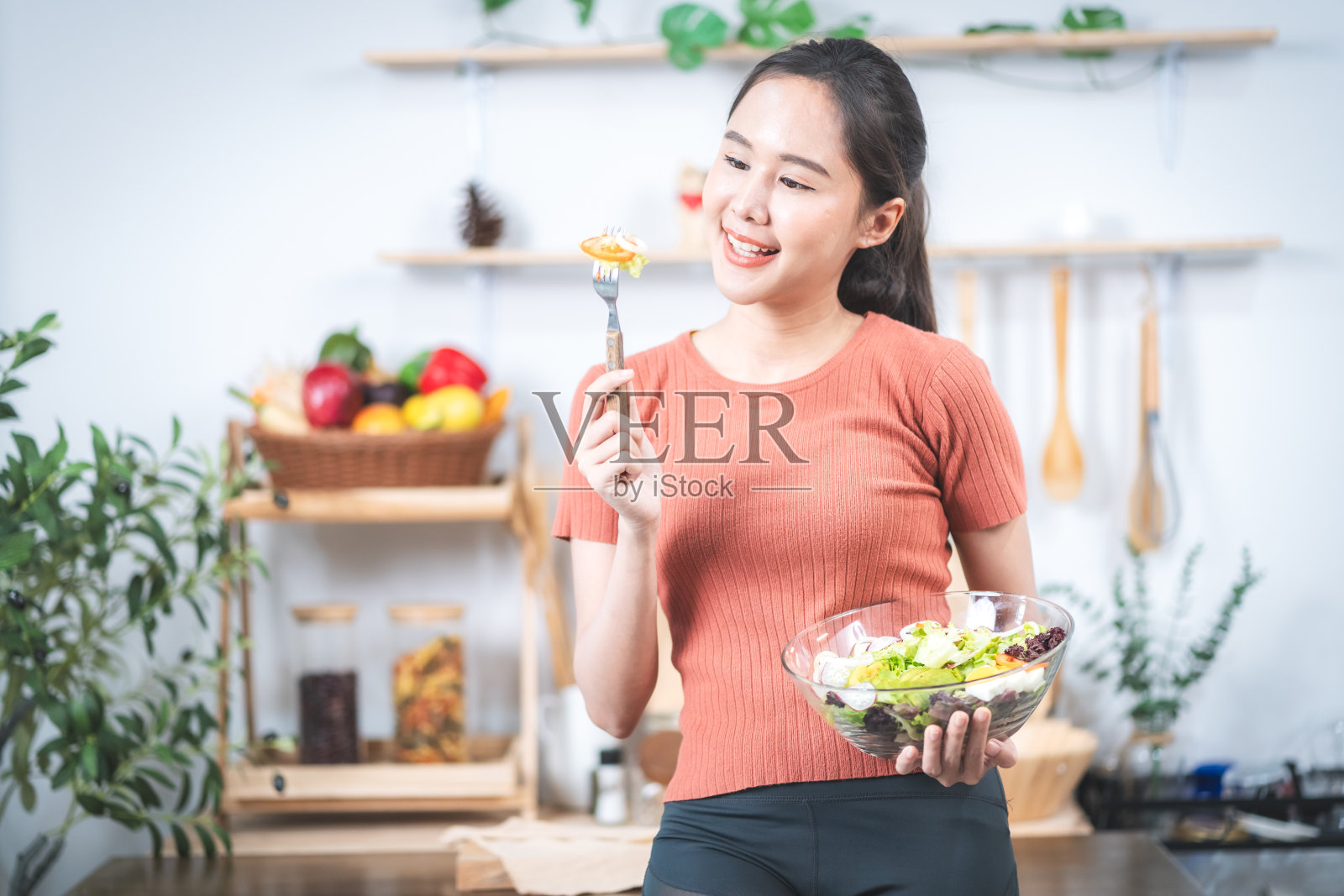 美丽健康的亚洲女人，穿着运动服，在厨房锻炼后，用健康的盘子吃沙拉和其他蔬菜。照片摄影图片