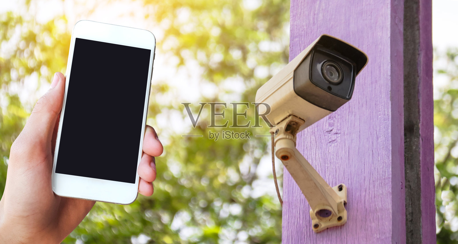 一只手拿着手机，放在一个家庭闭路电视摄像机的画面上。照片摄影图片