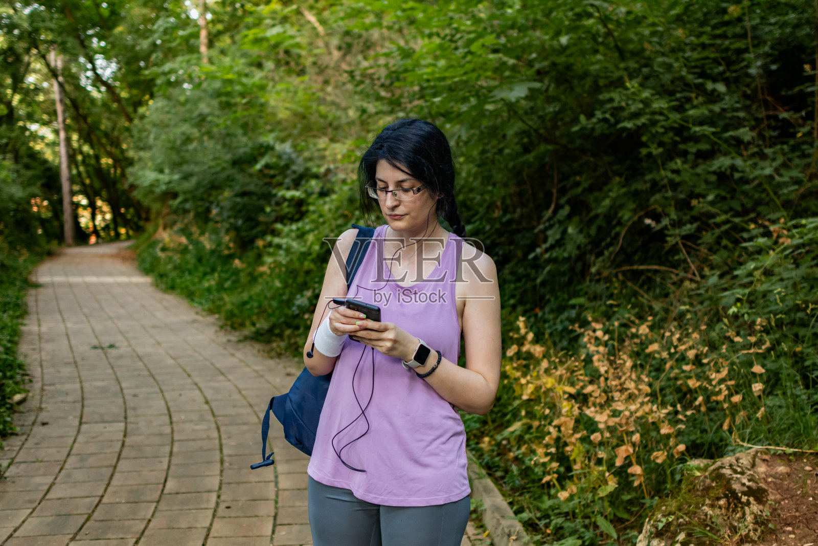 穿着健身服的年轻漂亮的女人在公园里做体育锻炼。她在训练前检查耳机。照片摄影图片