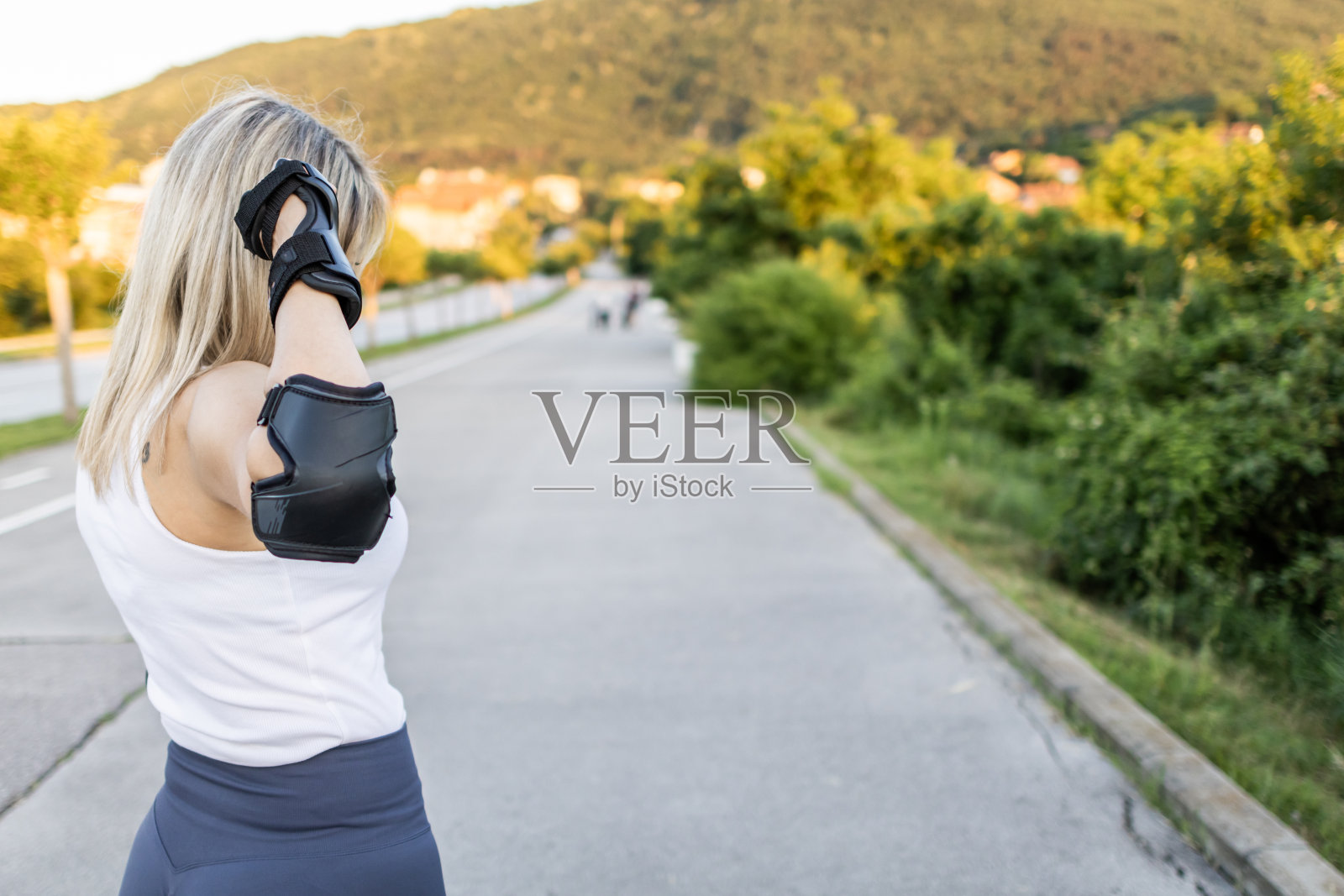 一个漂亮的金发女人的肖像，穿着直排轮滑站在路上。日落时分穿着运动服的迷人女运动员。照片摄影图片