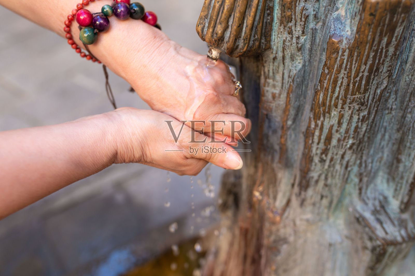 一位身份不明的老年妇女在公共饮水机里洗手。照片摄影图片