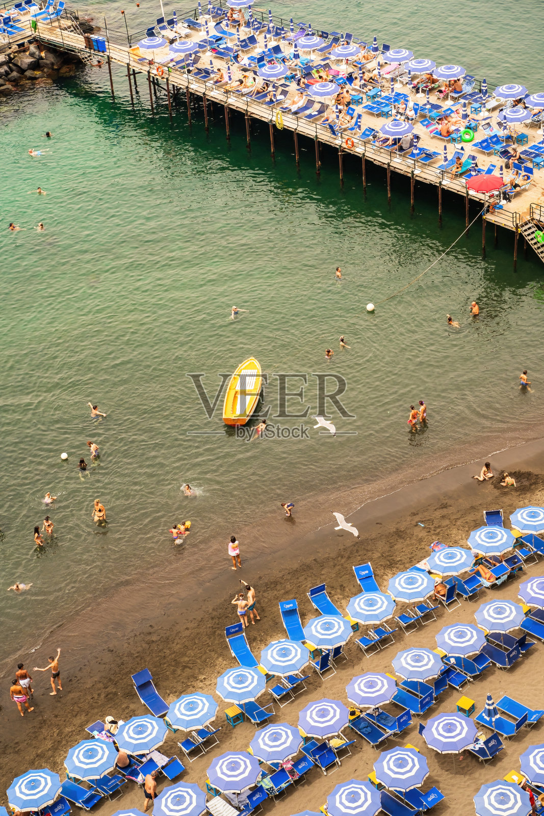 人们在码头的沙滩上放松，在索伦托的充气床和漂浮的船只上游泳照片摄影图片