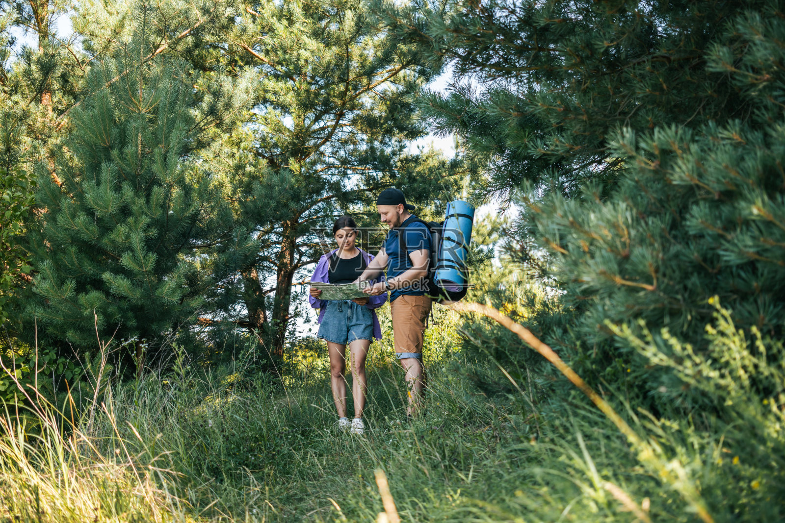 一对幸福的情侣背着背包，看着地图寻找正确的方向，在夏日的森林里散步照片摄影图片