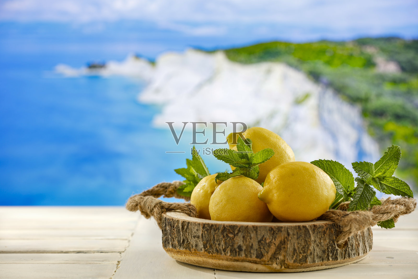 黄色柠檬散落在木制桌面与模糊的海景背景。照片摄影图片