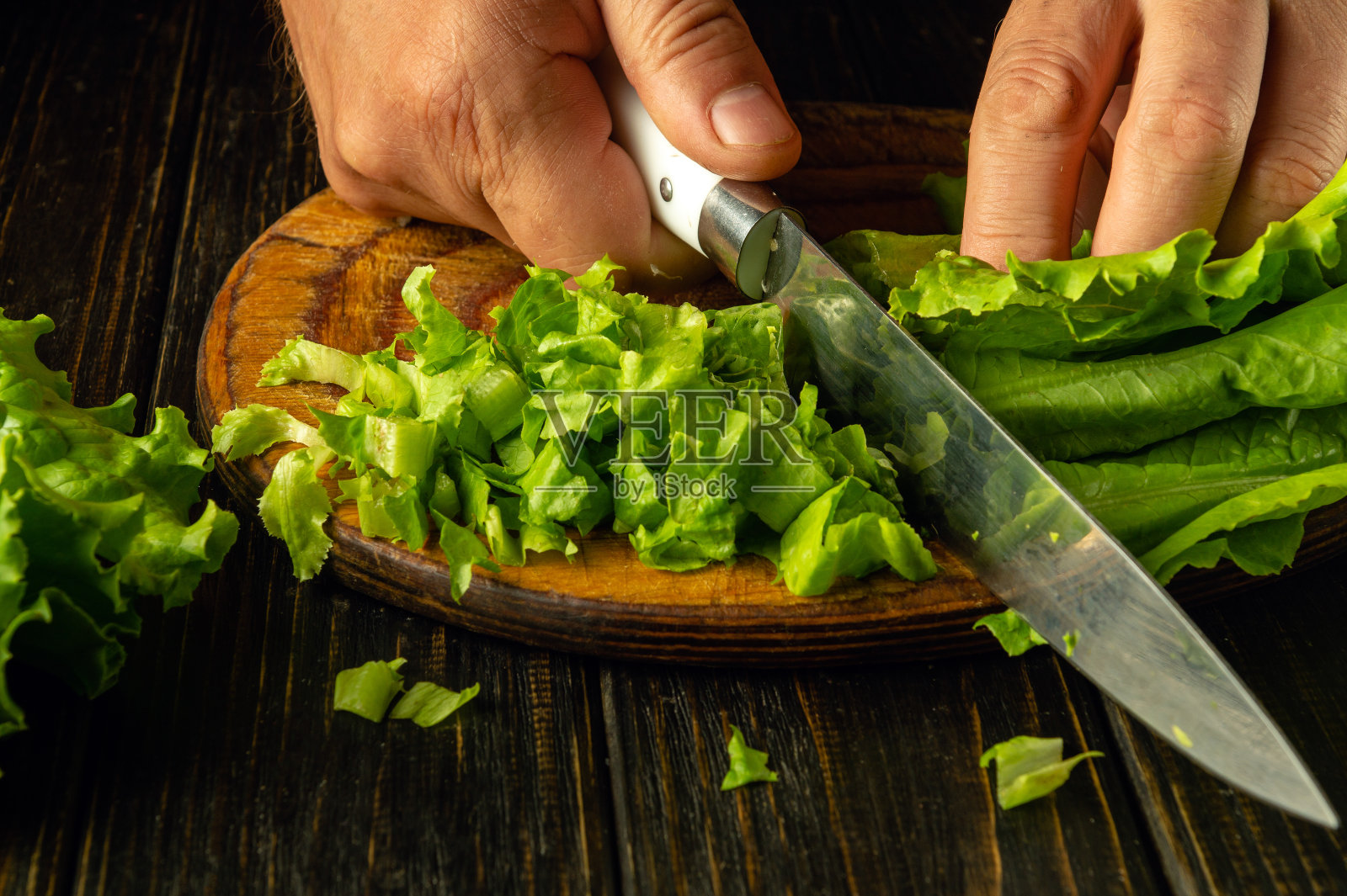 厨师手拿刀的特写。用厨师的手在菜板上切新鲜的生菜，准备美味的菜肴照片摄影图片