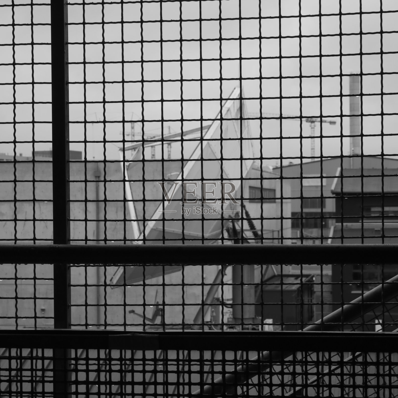 通过铁丝网拍摄的大型卫星天线。照片摄影图片