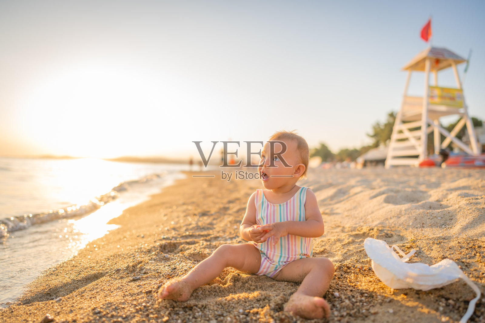 夏天戴着帽子的小女孩坐在沙滩上照片摄影图片