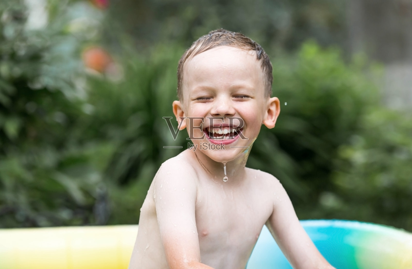 天气很热。一个可爱的男孩正在游泳池里游泳和溅水花。一个快乐的小男孩对着镜头微笑。水花四溅。暑假带孩子的概念。照片摄影图片