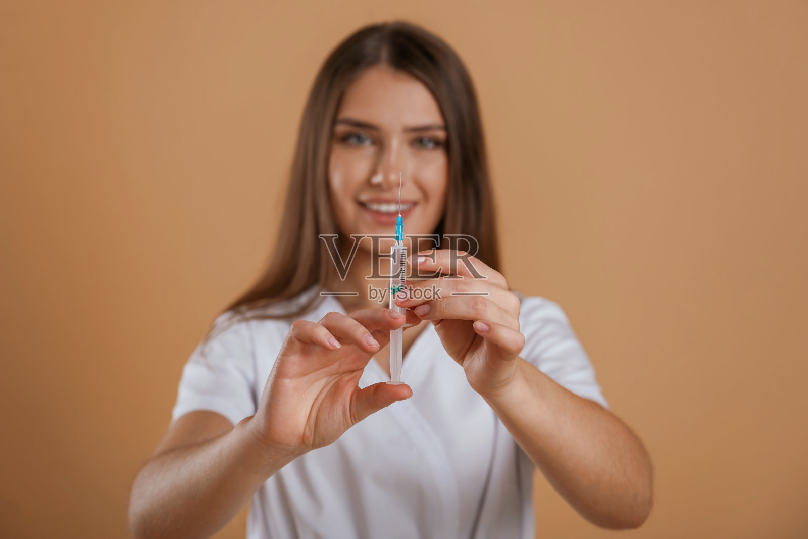 注射器在护士手中。年轻漂亮的女人在画室的背景下照片摄影图片