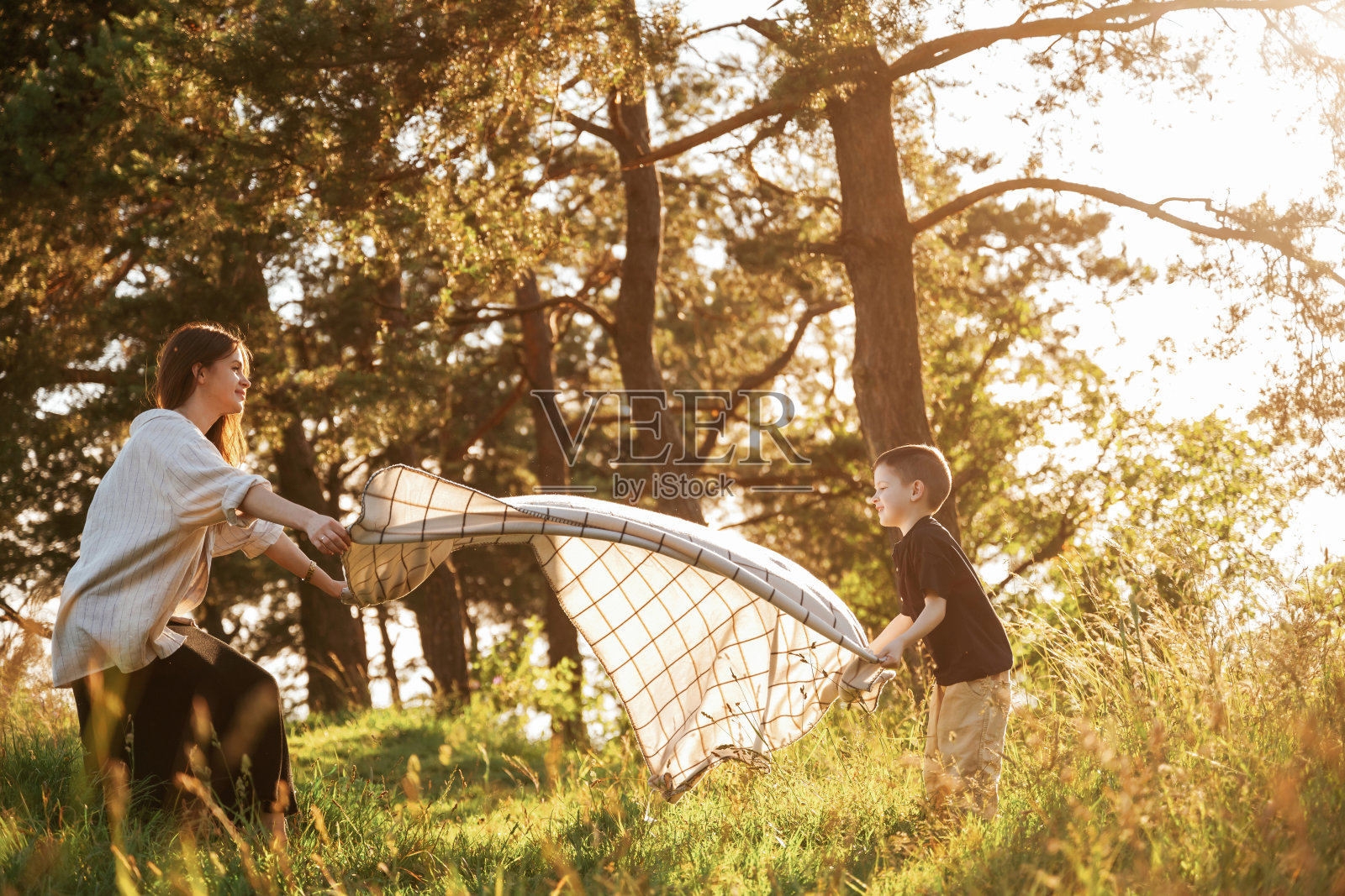 用毯子，把它放在地上。妈妈和儿子一起在森林里照片摄影图片