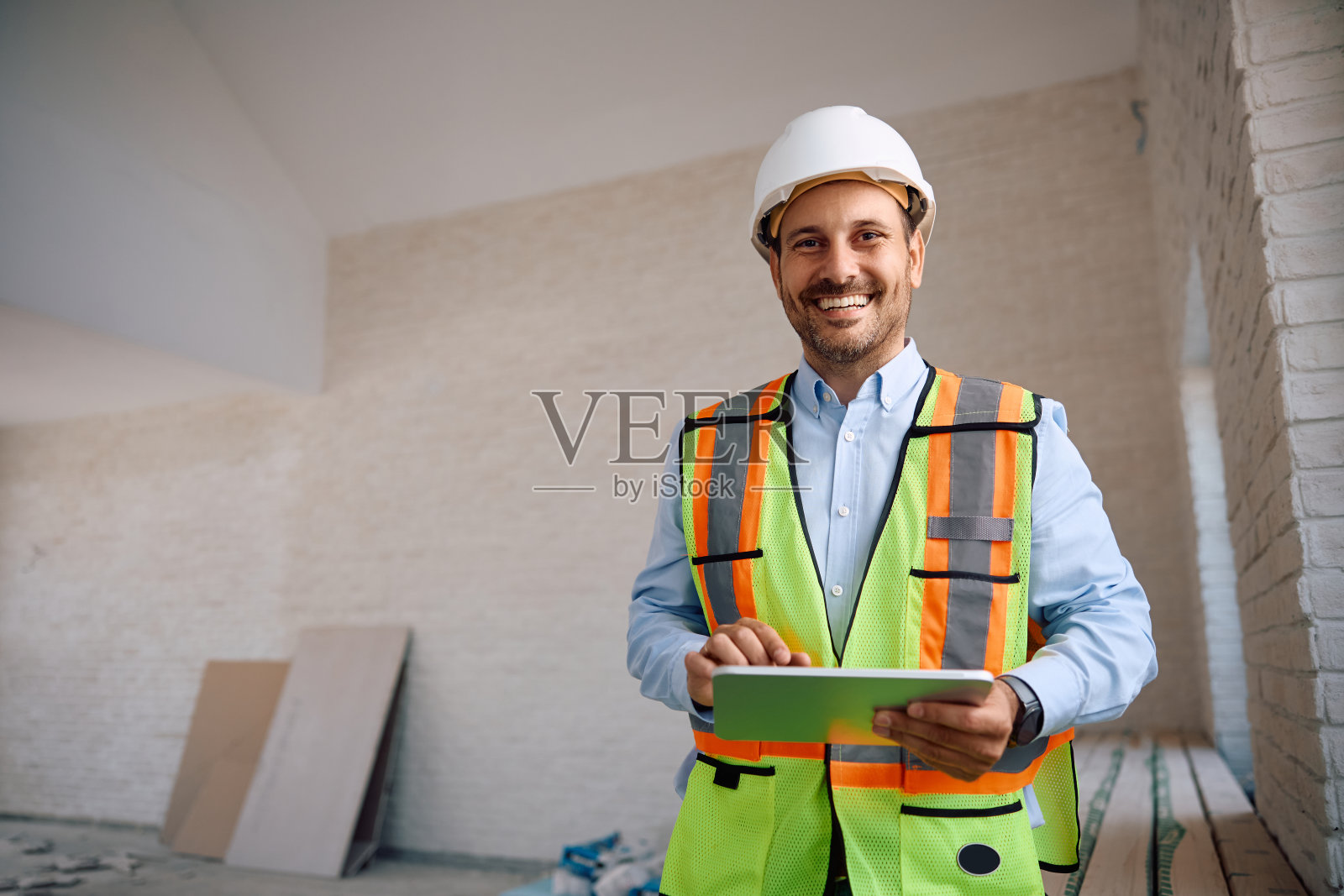 快乐的建筑师在建筑工地使用数码平板电脑，看着相机。照片摄影图片