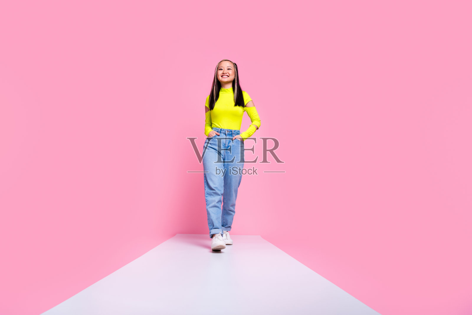 中国女孩染发的照片，穿着黄色高领毛衣，伸出舌头，在粉红色的背景上分开辫子照片摄影图片