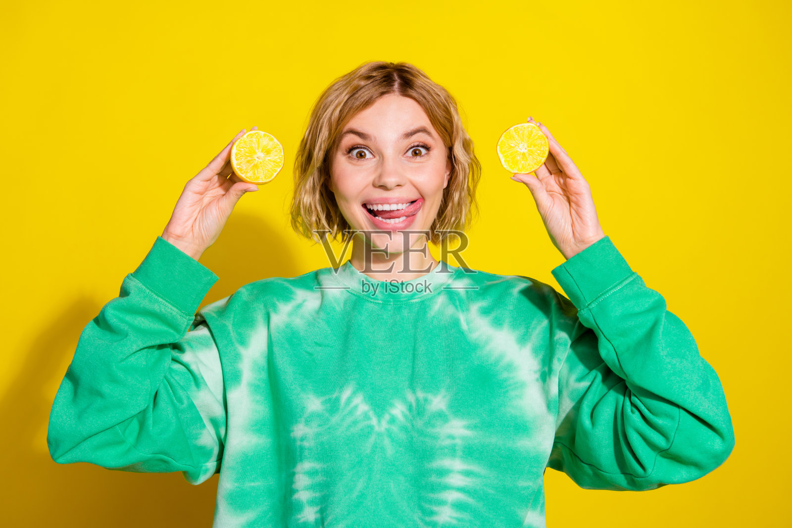 照片中光鲜迷人的女士穿着扎染运动衫突出，显示出两片柠檬片空空荡荡的黄色背景照片摄影图片