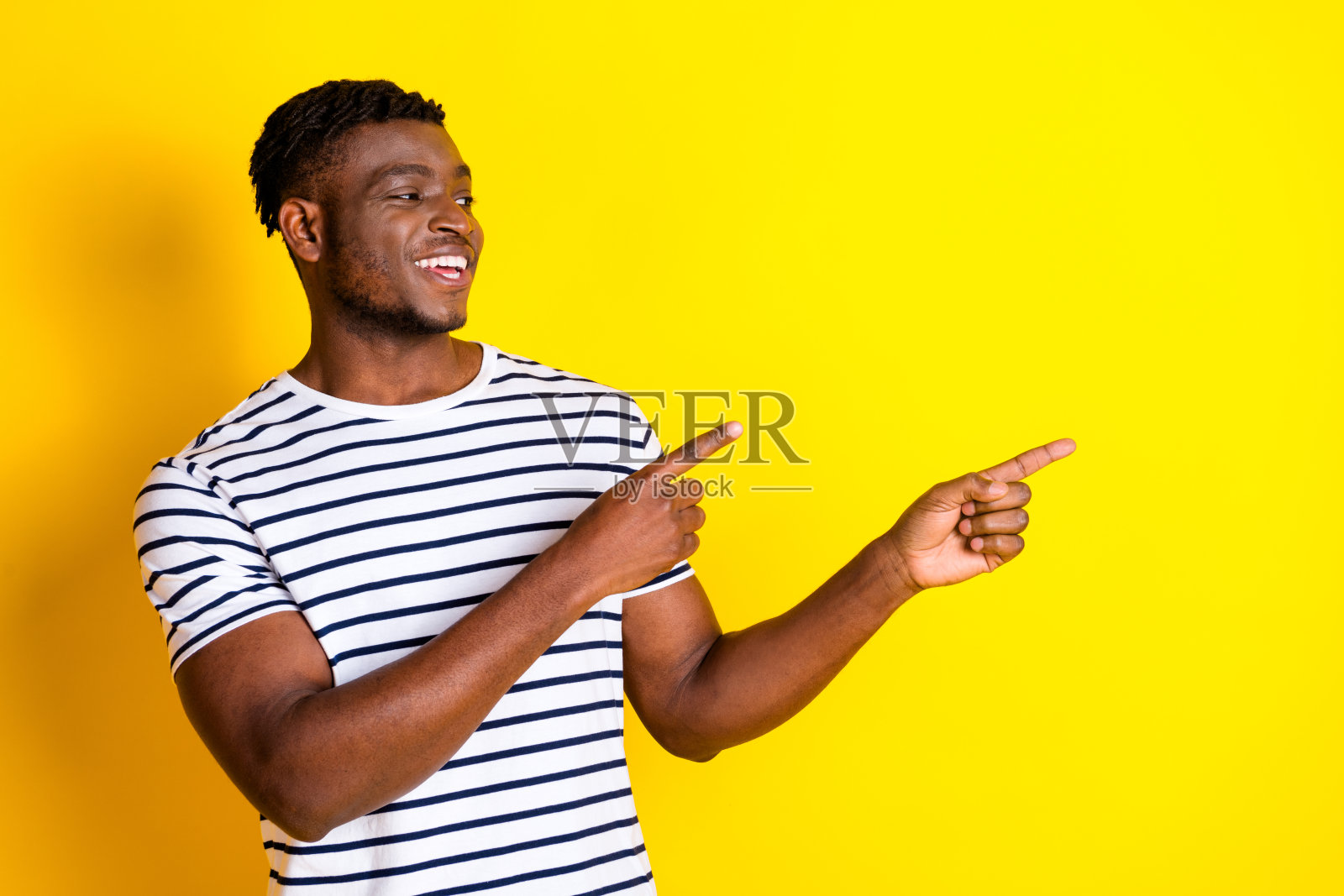 漂亮的年轻男子的肖像，手指指向空的空间，穿着条纹t恤，在充满活力的黄色背景上孤立照片摄影图片