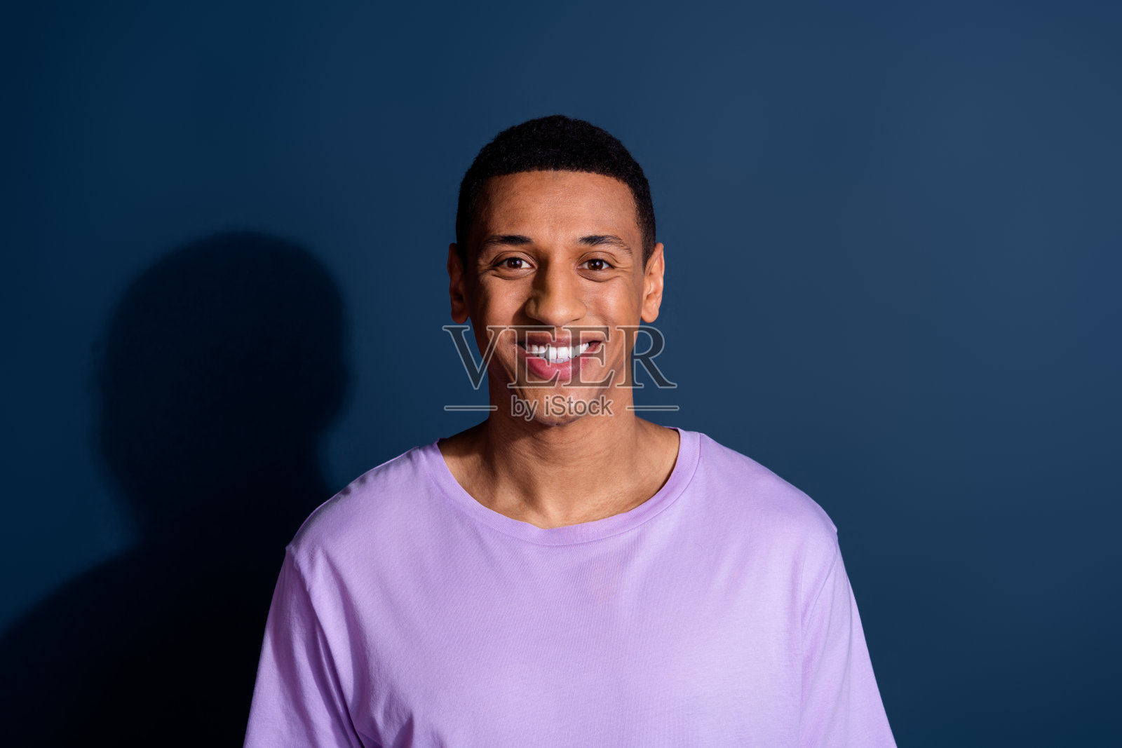 照片中，年轻风趣的小伙子露出灿烂的笑容，剪着短发，穿着时尚的紫色t恤，衬托着深蓝色的背景照片摄影图片