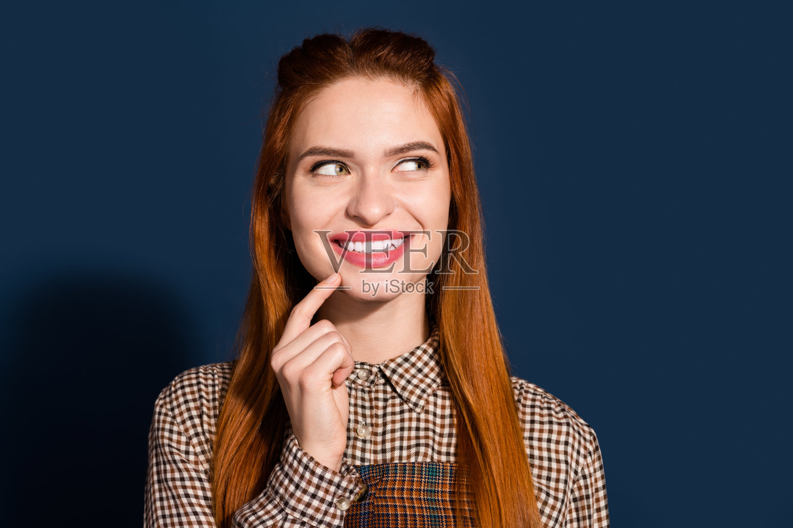 照片中开朗狡猾的女士穿着格子装，手指下巴看起来空白，孤立的深蓝色背景照片摄影图片