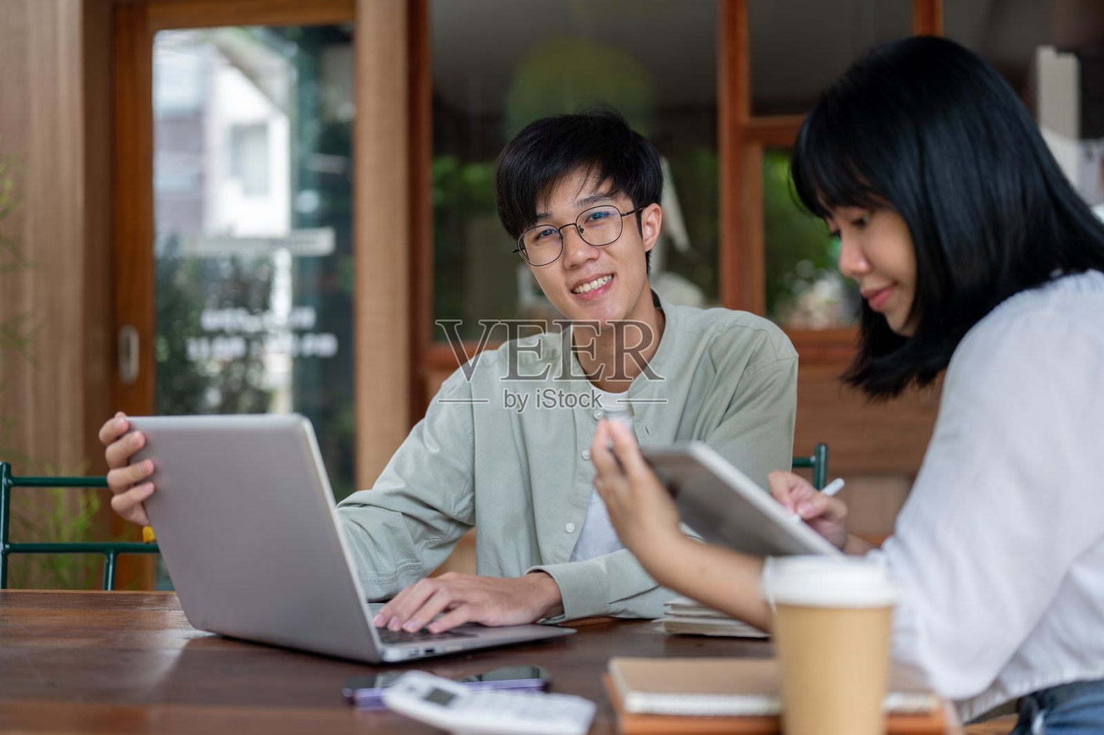 一个乐观的亚洲男人正在咖啡馆里和他的女同事远程工作，对着镜头微笑。照片摄影图片