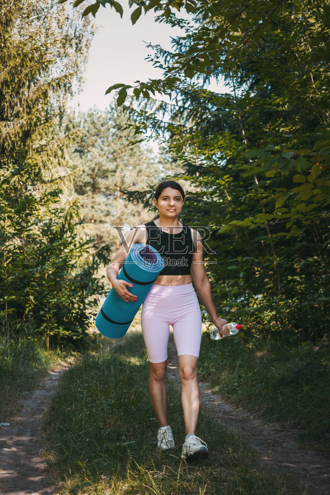 一个年轻的运动女子带着水瓶和健身垫在夏季公园散步，晨练的概念照片摄影图片