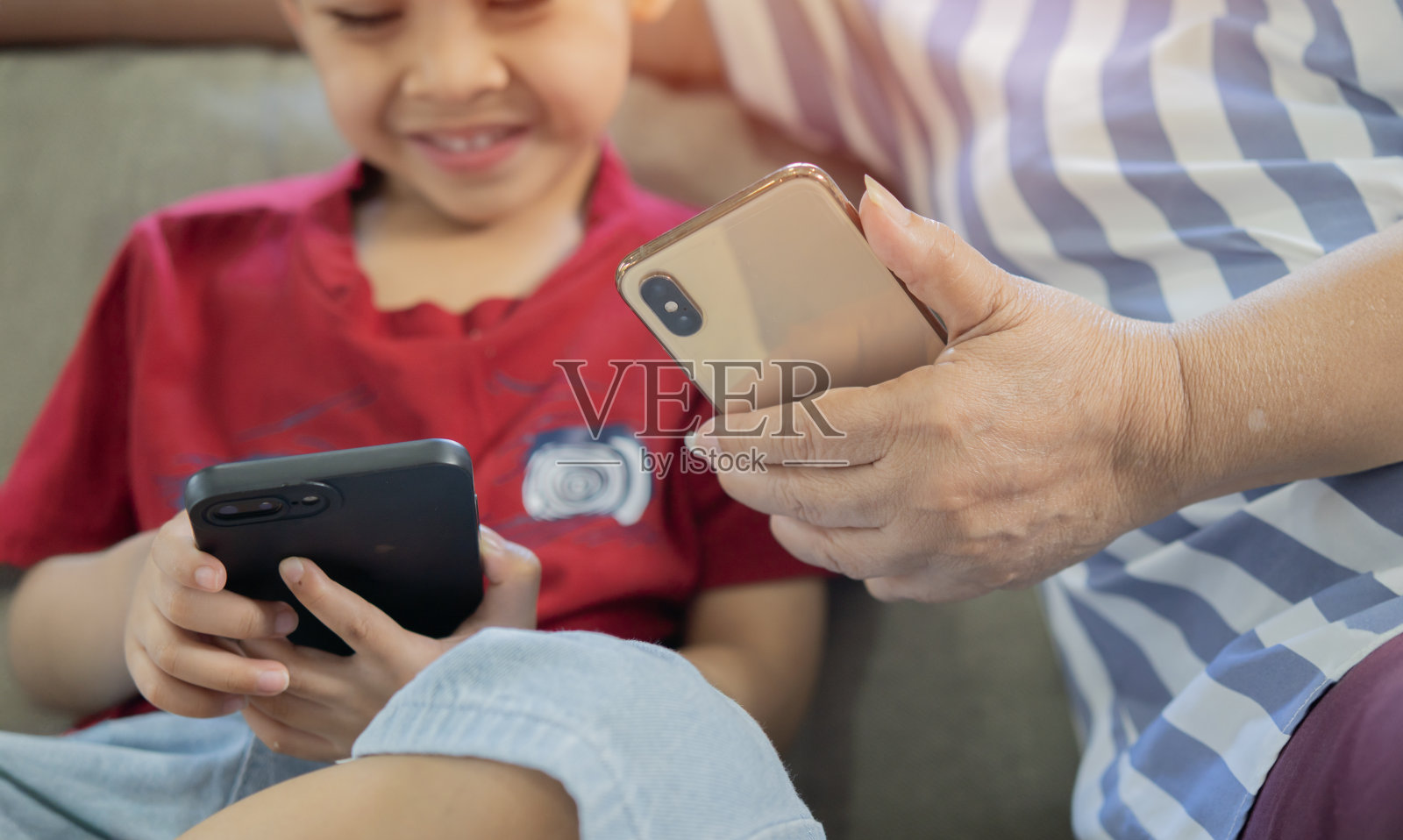 微笑的小男孩和老人坐在沙发上玩智能手机。照片摄影图片