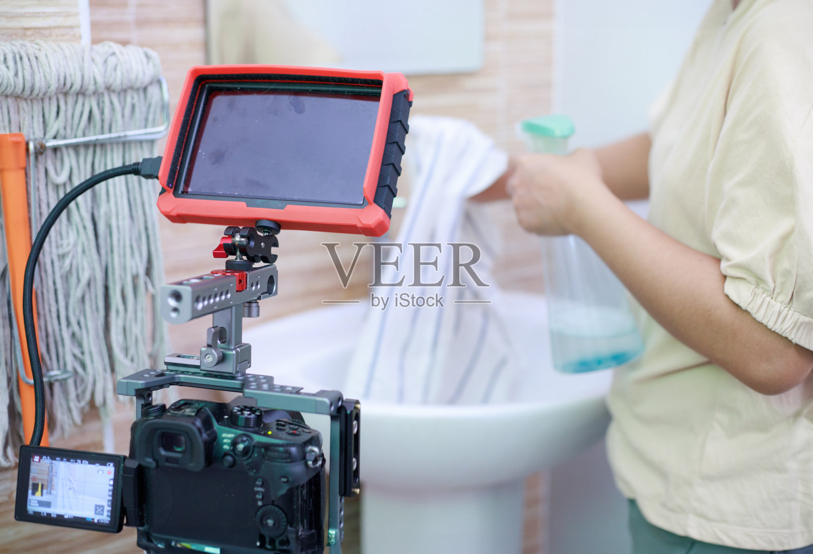 女人用布和喷雾清洁浴室水槽，并用相机记录照片摄影图片