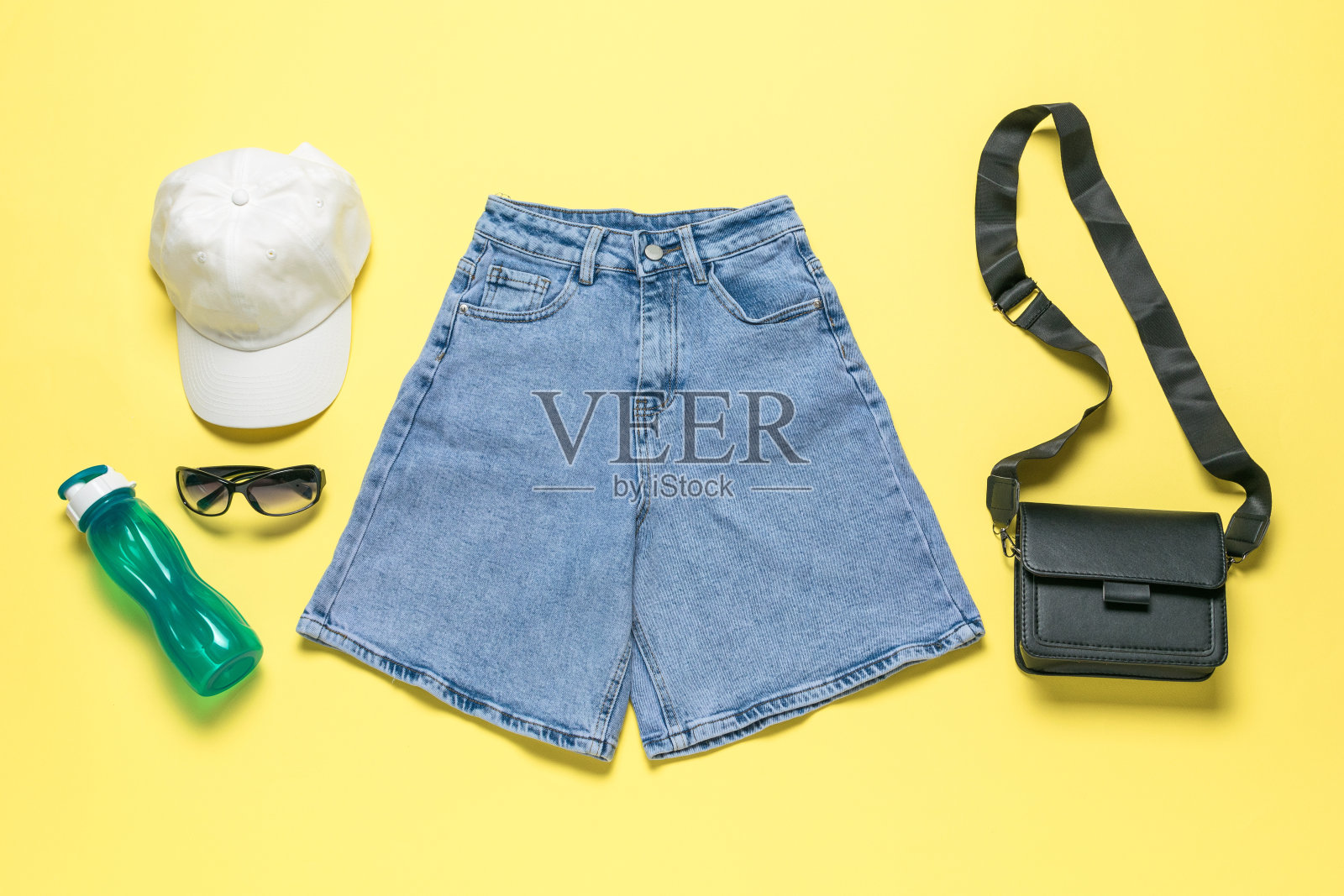夏季服装平面与牛仔短裤，配件，黄色背景的水瓶照片摄影图片