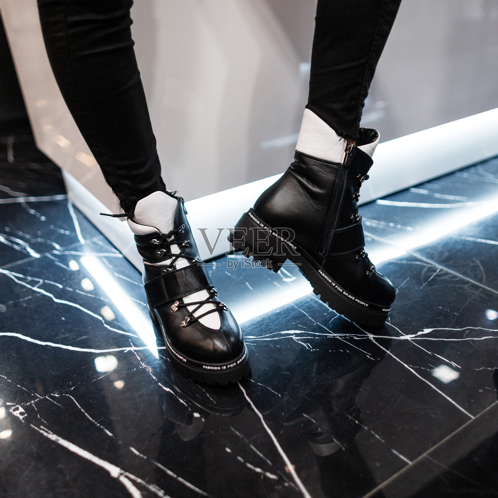 现代房间里穿着时髦的黑白皮靴的女性腿特写。穿着牛仔裤和时髦鞋子的时髦女孩站在商店里。休闲秋冬风格。时尚的新系列。照片摄影图片