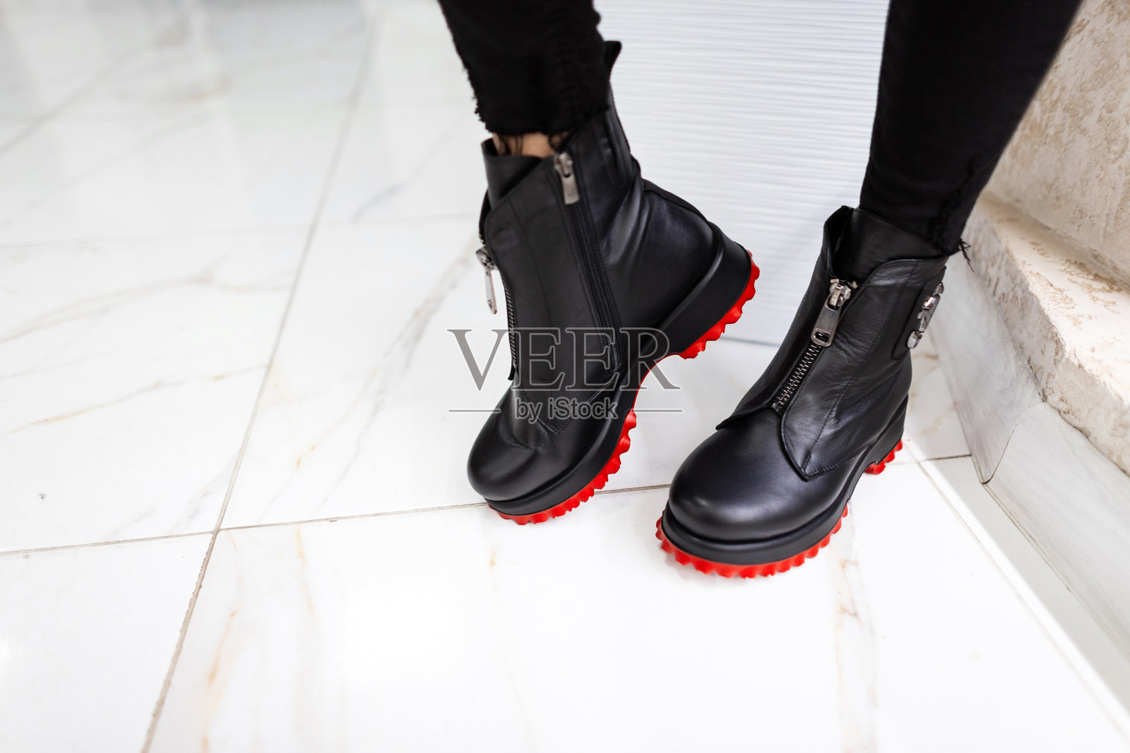 女性腿的特写，穿着时髦的黑色牛仔裤和红底的黑色皮靴。时髦的女人站在室内的瓷砖上。复古的风格。秋季时尚女鞋。照片摄影图片